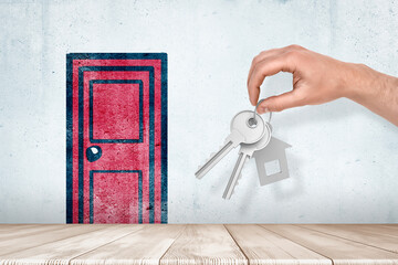 Hand holding silver keys with red cartoon door drawn on white wall background