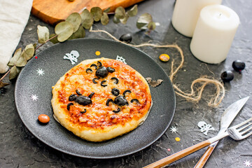 Halloween pizza with olive spiders. Halloween pizza on a plate on a dark background, next to the...