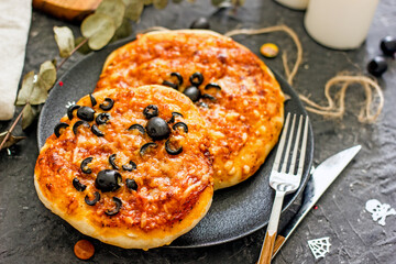 Halloween food pizza with olive spiders. Pizza for halloween on a plate on a dark background, near the cutlery. How to decorate a pizza for Halloween, scary food