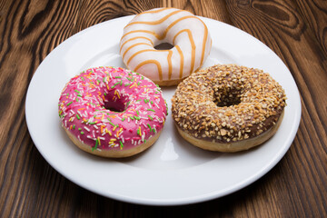Sweet donuts, cakes on a white plate and a wooden table