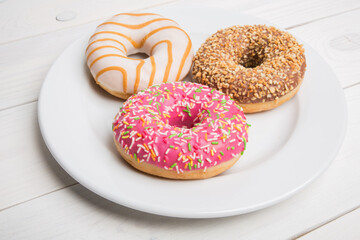 Sweet donuts, cakes on a white plate and a wooden table