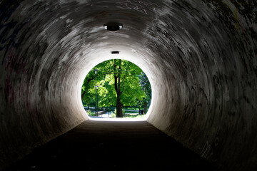 Dark concrete tunnel leading to a green park in the suburbs.