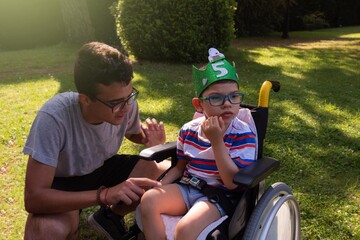 A child in a wheelchair with Pitthopkins syndrome celebrating his birthday with a handmade eva rubber wreath and a teenager taking care of him.