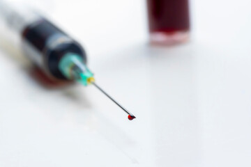 drop of blood on the tip of a syringe needle with an unfocused blood test tube in the background