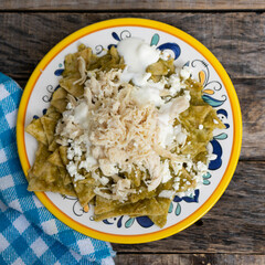Mexican green chilaquiles with chicken and cheese on wooden background