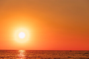 Person silhouette stand up paddle boarding at dusk on a flat quiet sea on sunset