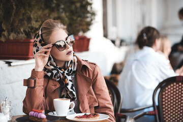 Beautiful woman 24-25 year old drinking coffee in cafe wearing stylish jacket, sun glasses and silk...