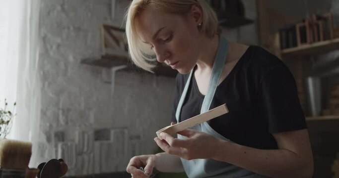 Woman carpenter polishes wooden spoon with a sandpaper close-up