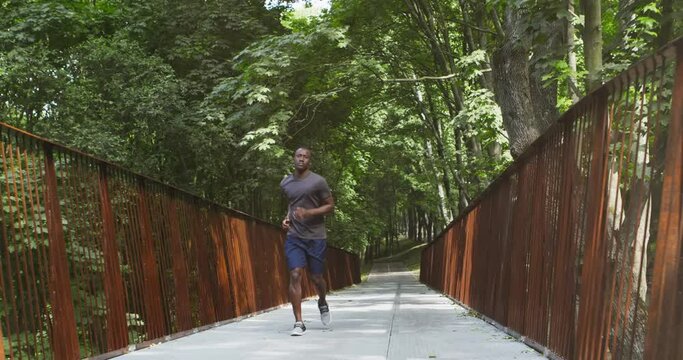 Active african american guy jogging on bridge in public park