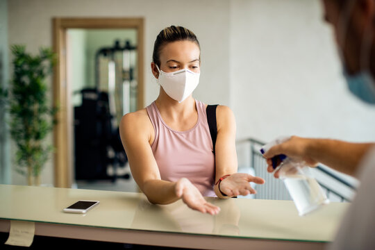Athletic woman with face mask getting her hands disinfected at health club.