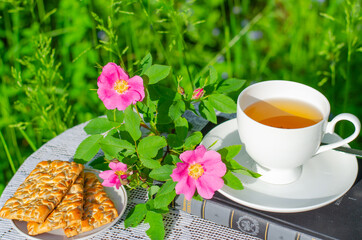 A Cup of green tea with a mint leaf, flowers, and a book on a table in the garden. Evening tea with cookies. Summer village concept. Copy space.