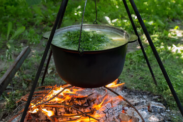 Black cauldron with soup with dill on a tripod over a bonfire