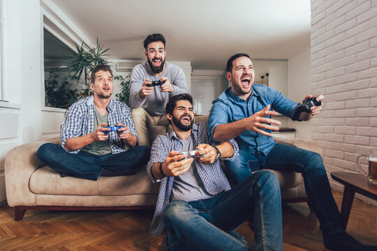 Smiling male friends playing video games at home and having fun.