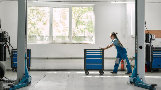 African American Woman, Professional Female Mechanic Pulling, Carrying Tool Box Cart In Auto Repair Shop. Car Service, Maintenance And People Concept