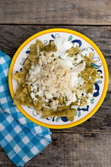 Mexican green chilaquiles with chicken and cheese on wooden background