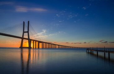 Naklejka na ściany i meble Beautiful sunrise at Vasco da Gama Bridge, the longest bridge in Europe, who spans the Tagus River in Lisbon, Portugal.