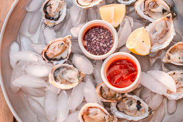 Oyster platter with minced shallot in red vinegar and horseradish tomato sauce. Seafood plate. Ocean meal. Raw seafood. Lemon slices. Fresh and nutritional dinner. Luxury meal. Fancy dinner.