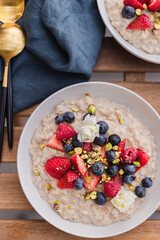 Healthy breakfast goals. Cooked oatmeal with seasonal berries, nuts and edible flowers. Nutritional meal. Organic food. Strawberries, blueberries, raspberries. Weekday brunch. Everyday meal. Oats.