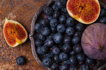 Ripe figs and blueberries in an old plate on a reddish-brown background. View from above