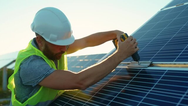 At sunlight man worker fixing solar panel to a metal basis with a drill in a sunny day green environmental rooftop construction engineer photovoltaic electricity battery utility slow motion