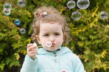 portrait of happy little beautiful girl blowing out soap bubbles on natural background. children's leisure. funny outdoor games