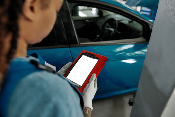 Young african american woman, professional female mechanic looking at the blank screen of tablet pc, using it at auto repair shop