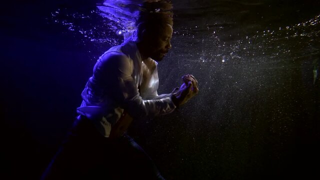 adult man is dancing underwater in pool, moving hands, male dancer