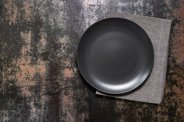 Empty black plate and napkin on dark rustic background with copy space for your text. Table setting.