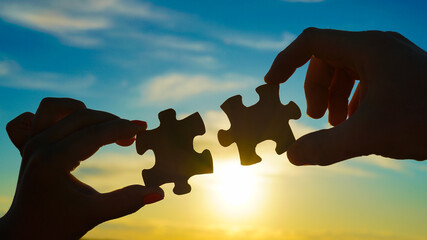 Two hands of businessmen connect puzzle pieces against the background of the sunset sky. Concept...