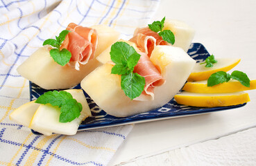 Grube plastry soczystego, słodkiego melona z szynką prosciutto ozdobione listkami mięty © Monika