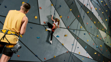 Male instructor teaching, looking at girl in safety equipment and harness while she is training on...