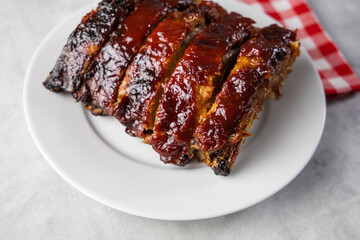 Oven-baked barbecue ribs with sauce on a white plate with a red checkered picnic napkin for a family barbecue