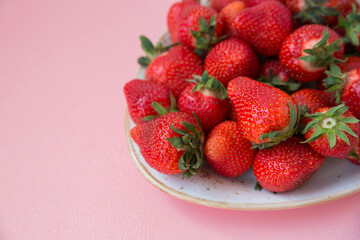 Ripe strawberries in a plate on a pink background