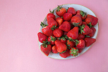 Ripe strawberries in a plate on a pink background