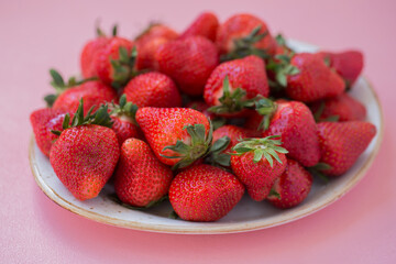 Ripe strawberries in a plate on a pink background