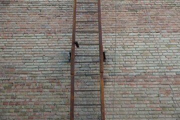 part of an old iron fire ladder in rust on a brown brick wall of a building on the street