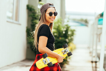 Fototapeta na wymiar Young positive woman carrying skateboard in the city