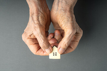 Inheritance concept. Elderly woman hands give a little toy house. Inherited property idea.