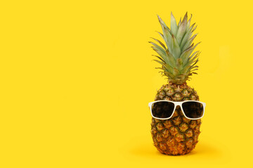 Pineapple with sunglasses against a bold yellow background. Minimal summer concept.