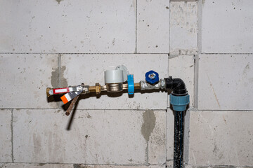 A temporary water valve with a meter connected to a pvc pipe, installed in a built house, against the wall.
