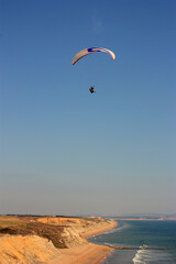 man is flying on white paraglider in the sky above the blue sea.. English canal, Barton-on-sea, England