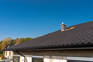 The roof of a single-family house covered with a new ceramic tile in anthracite, against the blue sky.