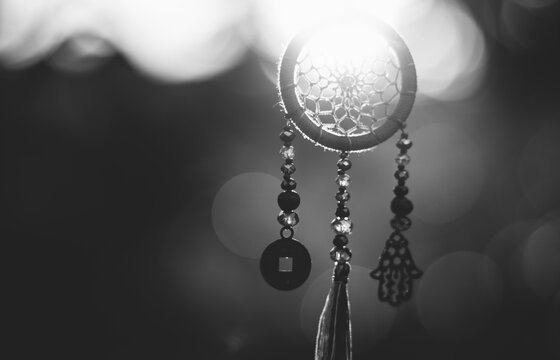 Monochrome close up of spiritual dreamcatcher necklace with sacred geometry circle with bokeh background backlit by sunset golden light