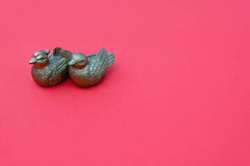 Figurines of mandarin ducks on pink background. Symbol of love in feng shui. Selective focus. Copy...