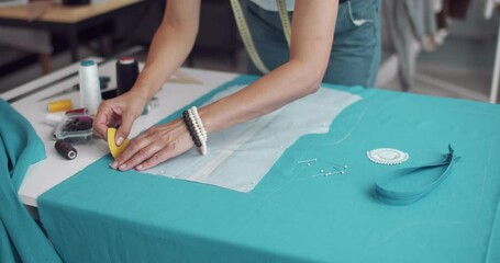 Close up of fashion designer chalking pattern on fabric according to client's parameters at atelier. Mature woman creating designer dress at workplace.