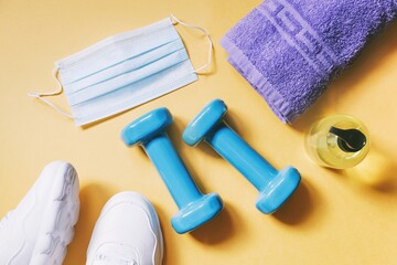 COVID-19 coronavirus post-lockdown. Resumption of work of fitness centers. Sports sneakers, dumbbells, blue disposable face mask, sanitizer gel and towel