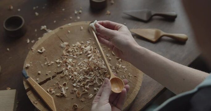 Woman carpenter varnishes wooden spoon with oil close-up