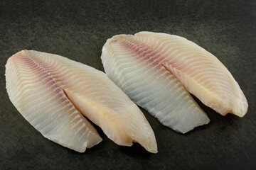 Fresh raw tilapia fish fillets on weathered black cutting board