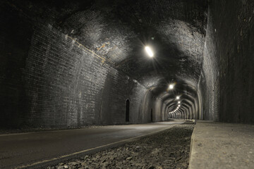 Road passes through dark grey brick tunnel lit by bars of light.