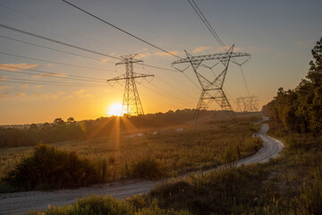 The sun rising behind a pair of towering electricity pylons